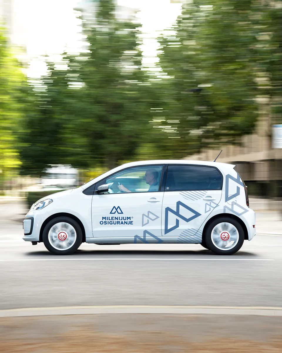 Beli automobil sa četvoro vrata na gradskoj ulici, sa plavim nalepnicama Milenijum osiguranje u različitim veličinama