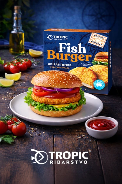 Pakovanje Tropic ribljeg burgera na stolu pored spremljenog burgera, zelene salate, maslinovog ulja i paradajza